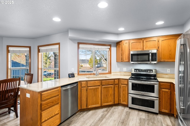 kitchen featuring light wood-style flooring, stainless steel appliances, a peninsula, a sink, and brown cabinetry