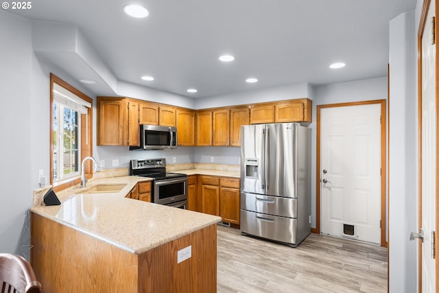 kitchen featuring recessed lighting, a peninsula, a sink, appliances with stainless steel finishes, and brown cabinetry