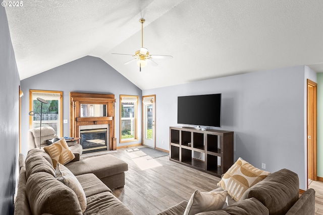 living area featuring a ceiling fan, vaulted ceiling, a textured ceiling, light wood-type flooring, and a fireplace