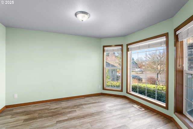 empty room with visible vents, a textured ceiling, baseboards, and wood finished floors