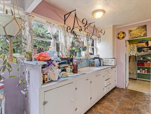 kitchen featuring white microwave, light countertops, a textured ceiling, white cabinetry, and a sink