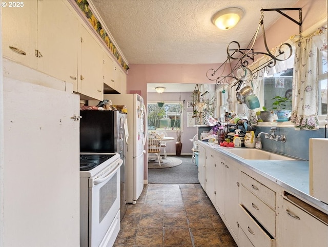 kitchen featuring light countertops, white cabinets, a sink, a textured ceiling, and white appliances