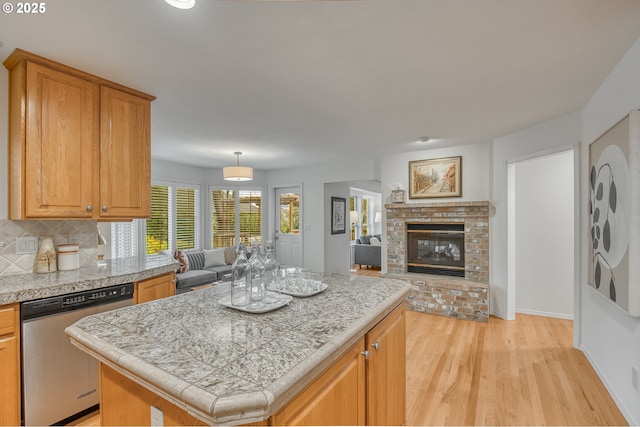 kitchen with a kitchen island, decorative backsplash, stainless steel dishwasher, light hardwood / wood-style floors, and a brick fireplace