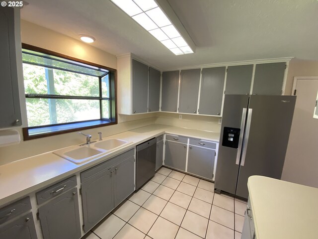 kitchen with gray cabinetry, dishwasher, light tile patterned floors, a sink, and stainless steel refrigerator with ice dispenser