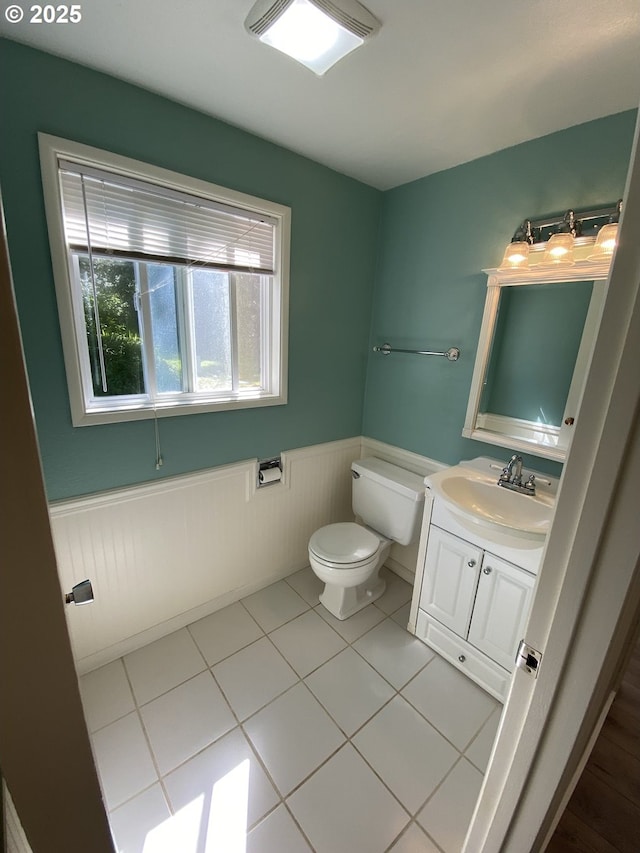 half bathroom with wainscoting, toilet, vanity, and tile patterned floors