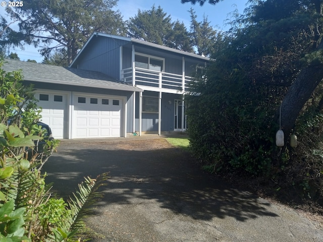 traditional-style home with a balcony, driveway, roof with shingles, and an attached garage