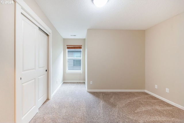 unfurnished bedroom featuring light colored carpet, a textured ceiling, and a closet