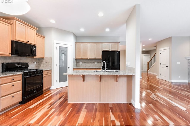 kitchen with light stone countertops, decorative backsplash, a kitchen breakfast bar, and black appliances