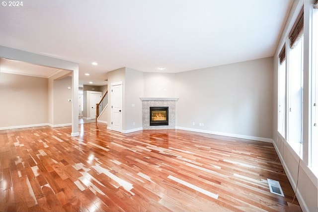 unfurnished living room with a healthy amount of sunlight, a tiled fireplace, and light hardwood / wood-style floors