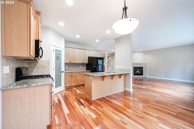 kitchen featuring sink, light hardwood / wood-style flooring, backsplash, black appliances, and light brown cabinets