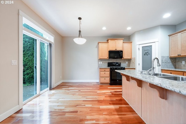 kitchen with light brown cabinetry, sink, a breakfast bar area, and black appliances