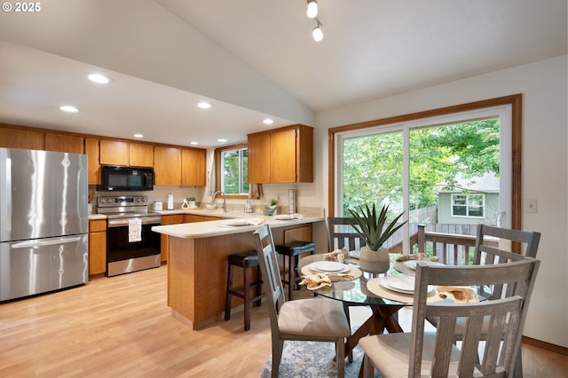 kitchen with stainless steel appliances, a sink, a peninsula, light countertops, and light wood-style floors