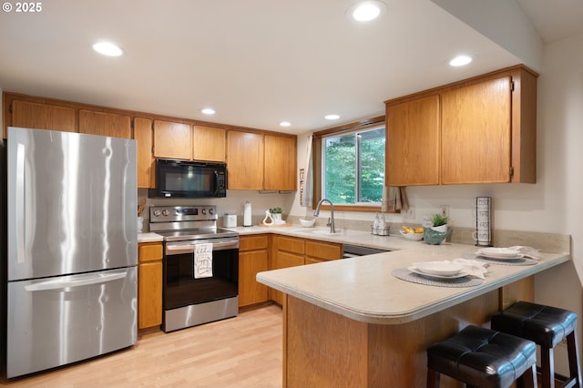 kitchen with appliances with stainless steel finishes, a sink, light countertops, a peninsula, and recessed lighting