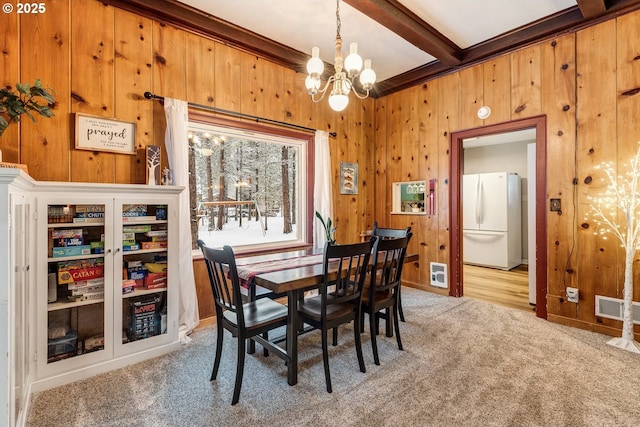 dining space with light carpet, wooden walls, a chandelier, and visible vents