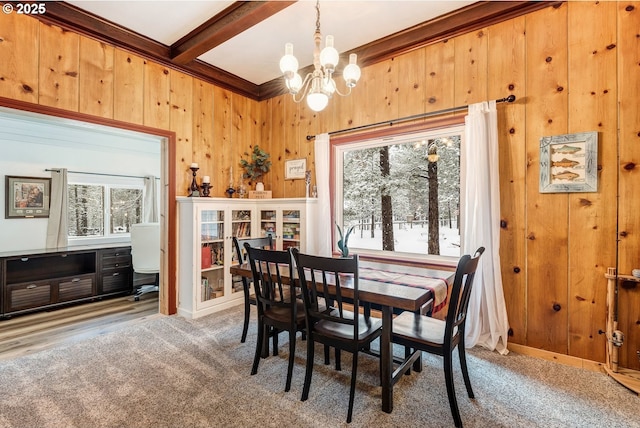 dining room with beamed ceiling, carpet flooring, wooden walls, and a notable chandelier