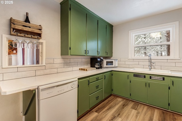 kitchen with a sink, white appliances, light wood-type flooring, backsplash, and light countertops