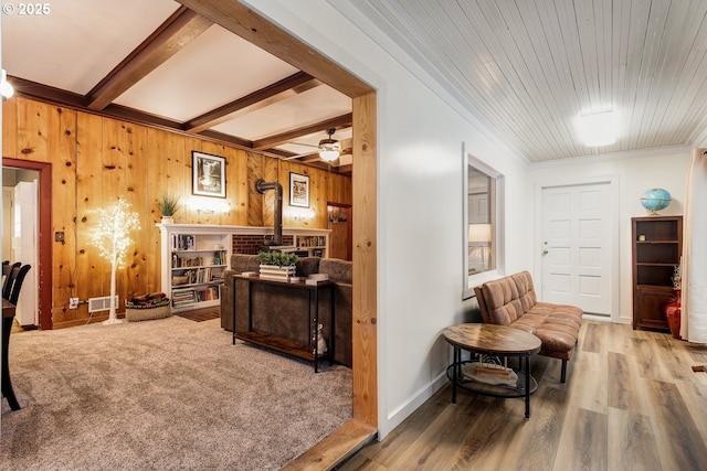 living area featuring hardwood / wood-style flooring, ceiling fan, wooden walls, beamed ceiling, and a wood stove