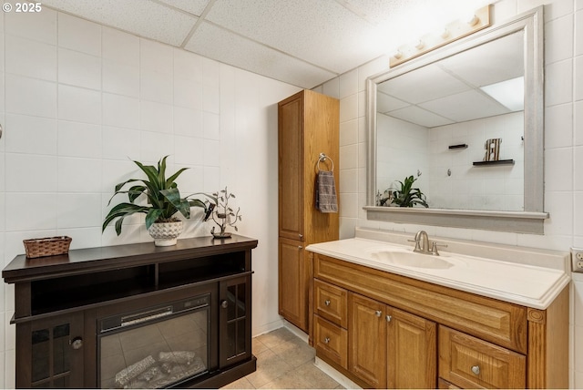 bathroom featuring tile patterned flooring, vanity, tile walls, and a drop ceiling