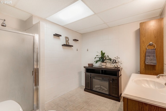 bathroom with toilet, a shower with shower door, a paneled ceiling, vanity, and tile patterned flooring