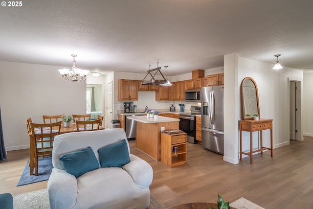 kitchen with light wood-type flooring, a notable chandelier, a kitchen island, stainless steel appliances, and light countertops