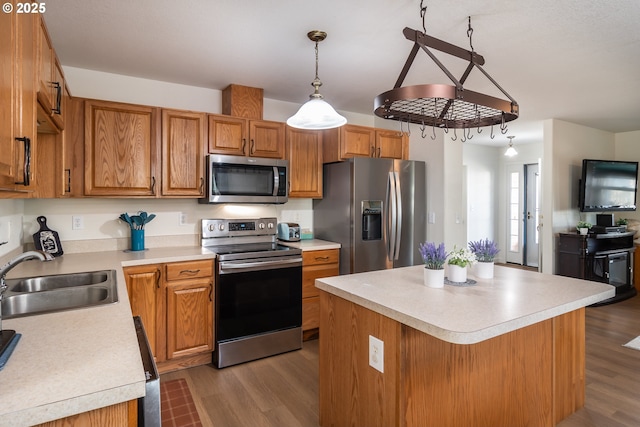 kitchen featuring a sink, wood finished floors, appliances with stainless steel finishes, light countertops, and hanging light fixtures