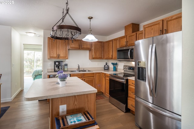 kitchen with wood finished floors, a sink, stainless steel appliances, light countertops, and a center island