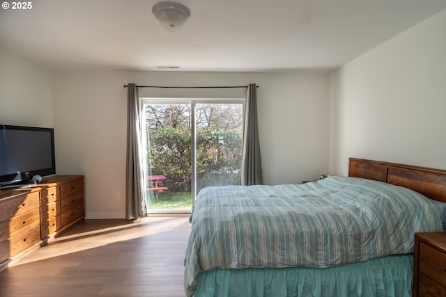 bedroom with visible vents, baseboards, wood finished floors, and access to outside