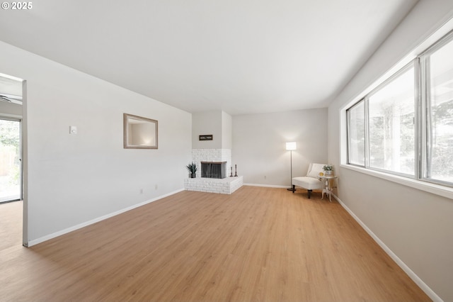 unfurnished living room with light wood-type flooring, baseboards, and a brick fireplace