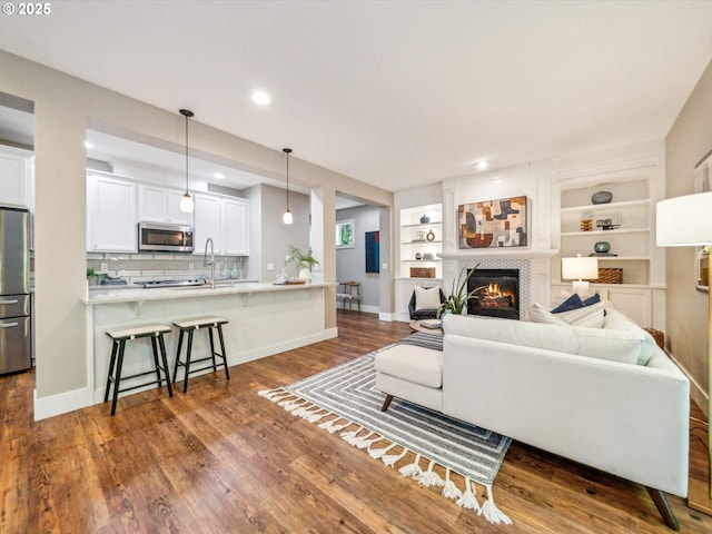 living room featuring recessed lighting, baseboards, a glass covered fireplace, and dark wood-style flooring