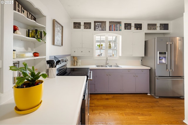 kitchen with a sink, light countertops, appliances with stainless steel finishes, open shelves, and light wood finished floors