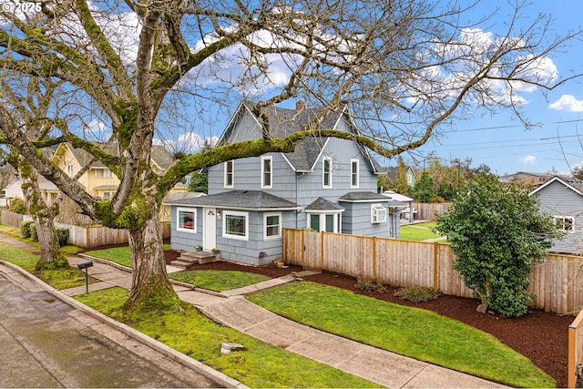 view of front of property featuring a shingled roof, a fenced front yard, and a front lawn