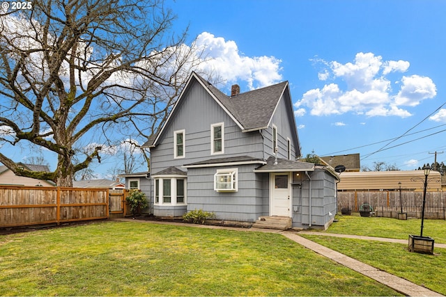 rear view of property with roof with shingles, a lawn, a chimney, and a fenced backyard