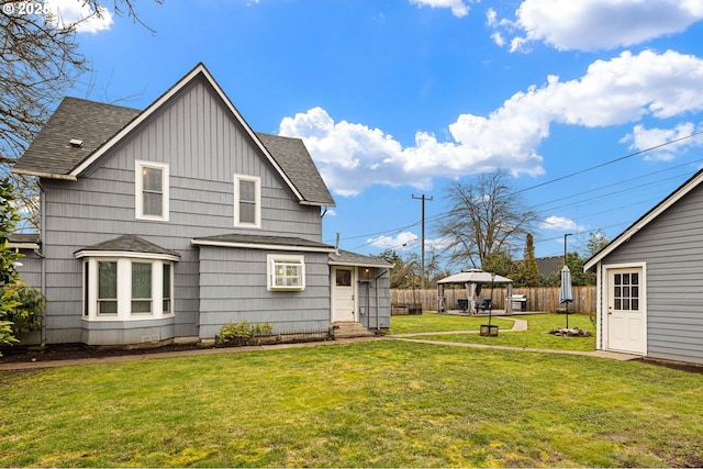 rear view of property with roof with shingles, fence, a gazebo, and a lawn