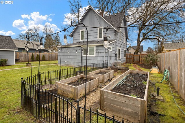 rear view of house with a yard, a shingled roof, a fenced backyard, and a garden