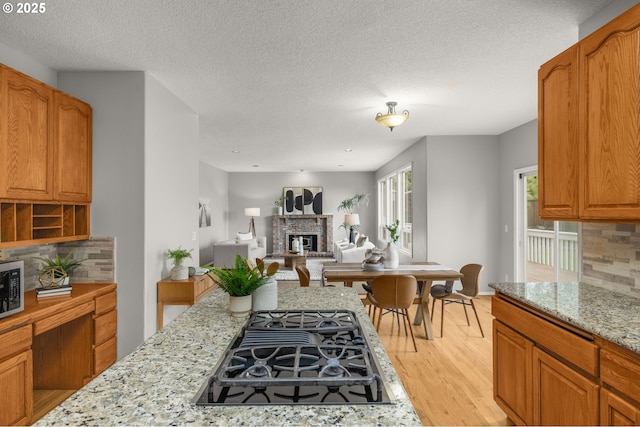 4025 Horton Rd, West Linn, OR 97068 - kitchen featuring black gas cooktop, light wood-type flooring, a brick fireplace, tasteful backsplash, and light stone countertops