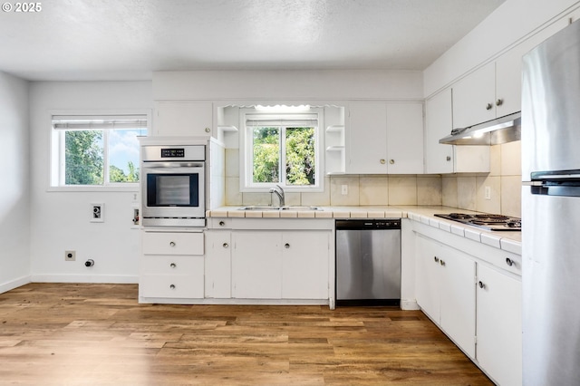2210 Winter St SE, Salem, OR 97302 - kitchen featuring stainless steel appliances, tile countertops, under cabinet range hood, open shelves, and white cabinets