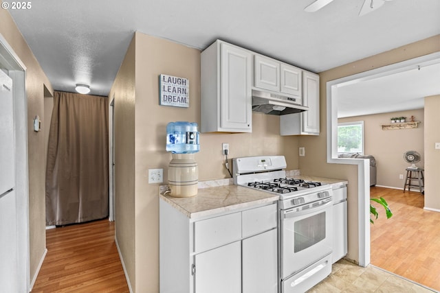 730 23rd St, Springfield, OR 97477 - kitchen featuring white range with gas stovetop, under cabinet range hood, light countertops, white cabinets, and light wood finished floors