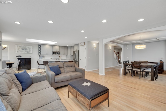 living room featuring arched walkways, recessed lighting, a notable chandelier, baseboards, and light wood finished floors