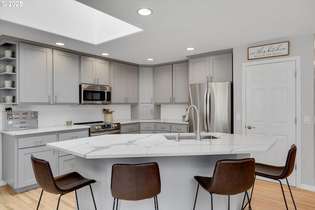 kitchen with open shelves, gray cabinets, stainless steel appliances, and a sink