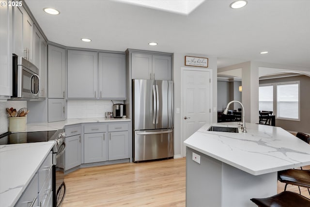 kitchen with appliances with stainless steel finishes, gray cabinets, a kitchen island with sink, and a sink