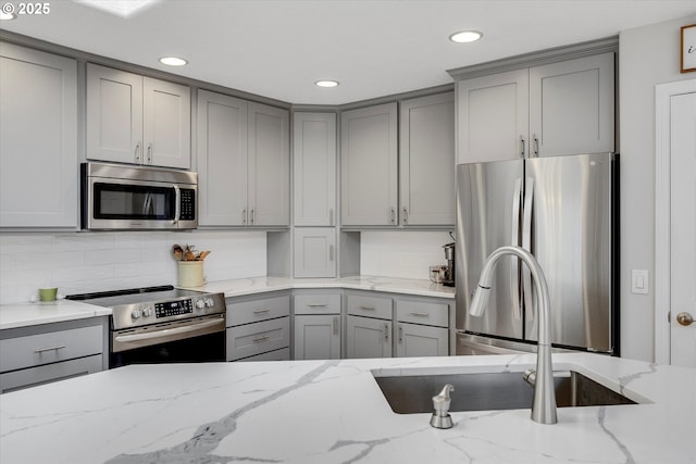 kitchen with stainless steel appliances, light stone counters, gray cabinets, and decorative backsplash