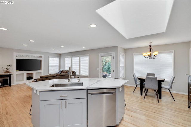 kitchen featuring hanging light fixtures, stainless steel dishwasher, open floor plan, a kitchen island with sink, and a sink