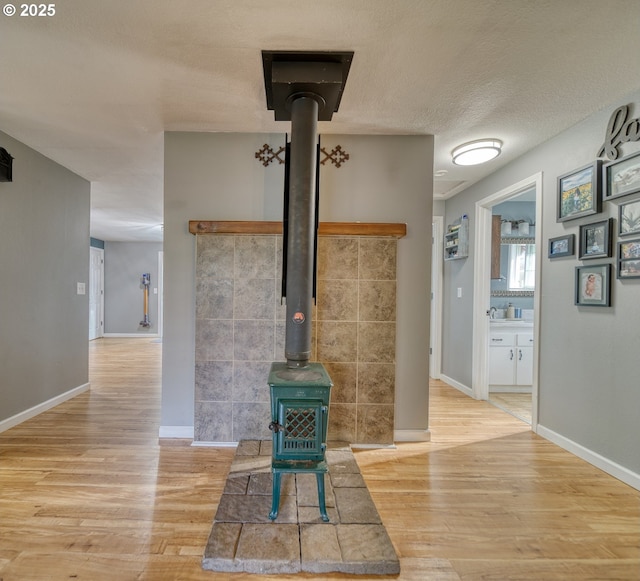 unfurnished living room featuring a wood stove, a textured ceiling, baseboards, and wood finished floors