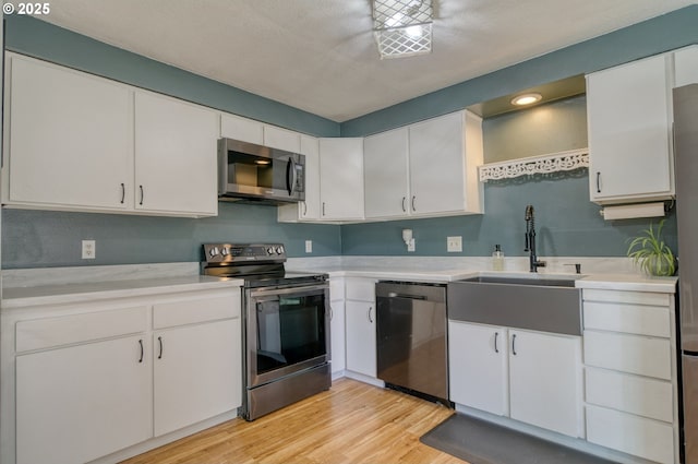 kitchen with stainless steel appliances, light wood-type flooring, light countertops, and a sink