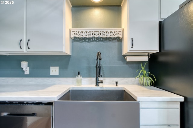 kitchen featuring dishwashing machine, light countertops, freestanding refrigerator, and white cabinets