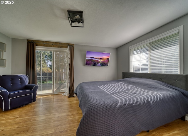 bedroom with access to outside, multiple windows, a textured ceiling, and wood finished floors