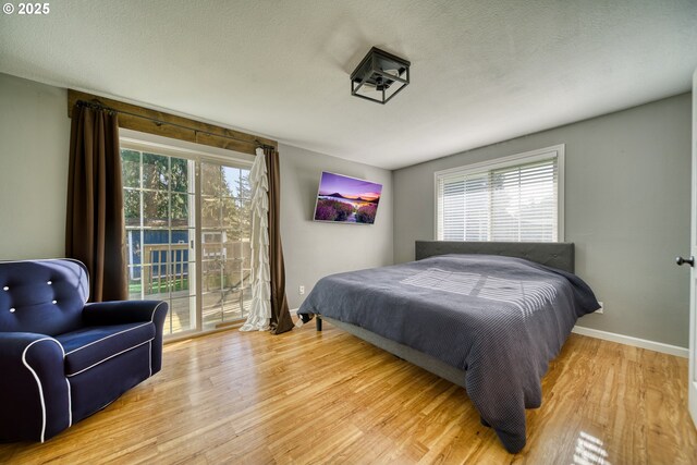 bedroom featuring access to exterior, a textured ceiling, baseboards, and wood finished floors