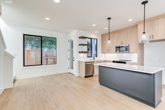 kitchen with stainless steel appliances, light countertops, a center island, light brown cabinetry, and pendant lighting