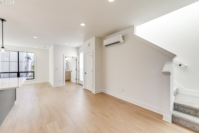 unfurnished living room with recessed lighting, baseboards, an AC wall unit, stairway, and light wood-type flooring