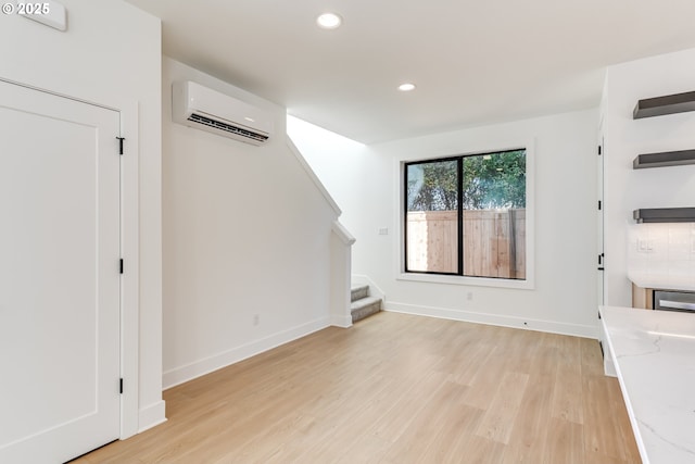 unfurnished living room featuring recessed lighting, a wall mounted AC, light wood-style floors, baseboards, and stairs